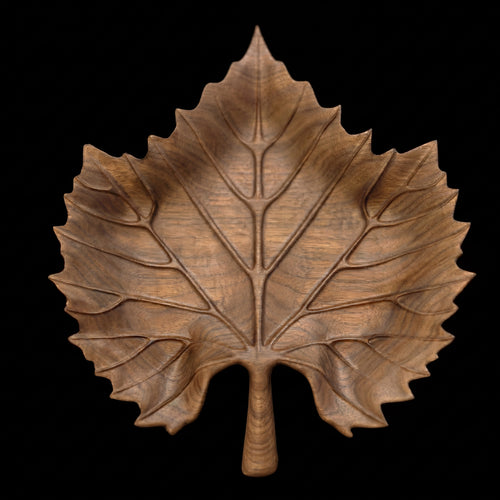 Фронтален изглед на дървено плато с форма на лист на черен фон, подчертаващ симетрията и шарката на ореха